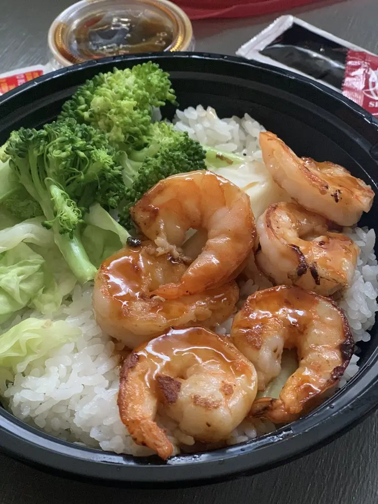 Yummy-Hawaiian-BBQ-Hawaiian-Restaurant-Teriyaki-Shrimp-Rice-Petaluma Teriyaki shrimp rice in a black container. Several shrimps with teriyaki sauce are on the rice, accompanied by broccoli at Yummy Hawaiian BBQ, a Hawaiian Restaurant in Petaluma